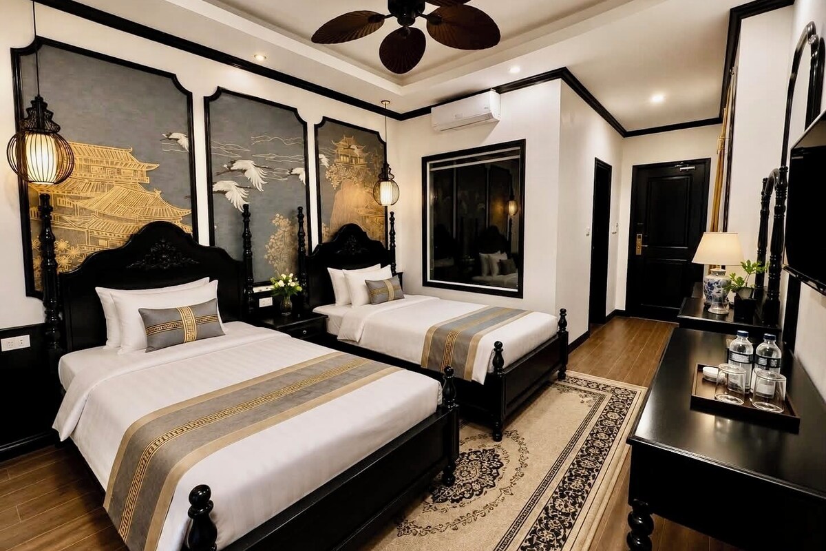 A hotel room with two beds, a large mirror, a ceiling fan, and artwork on the walls.