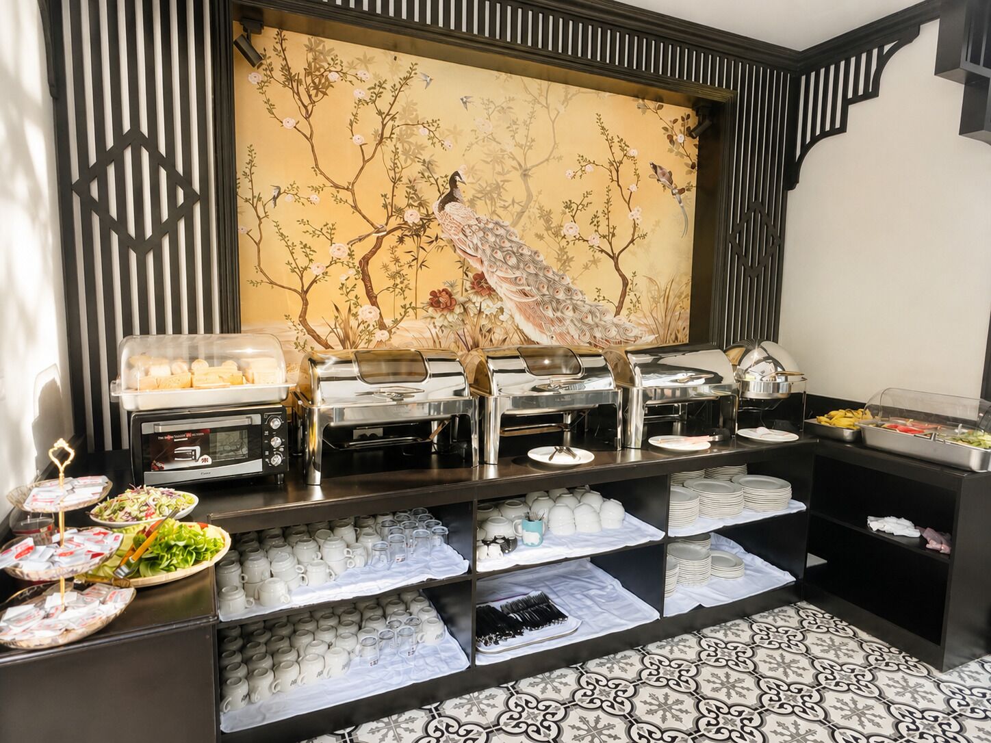 Un tavolo da buffet con diversi cibi e una parete decorata con un pavone.