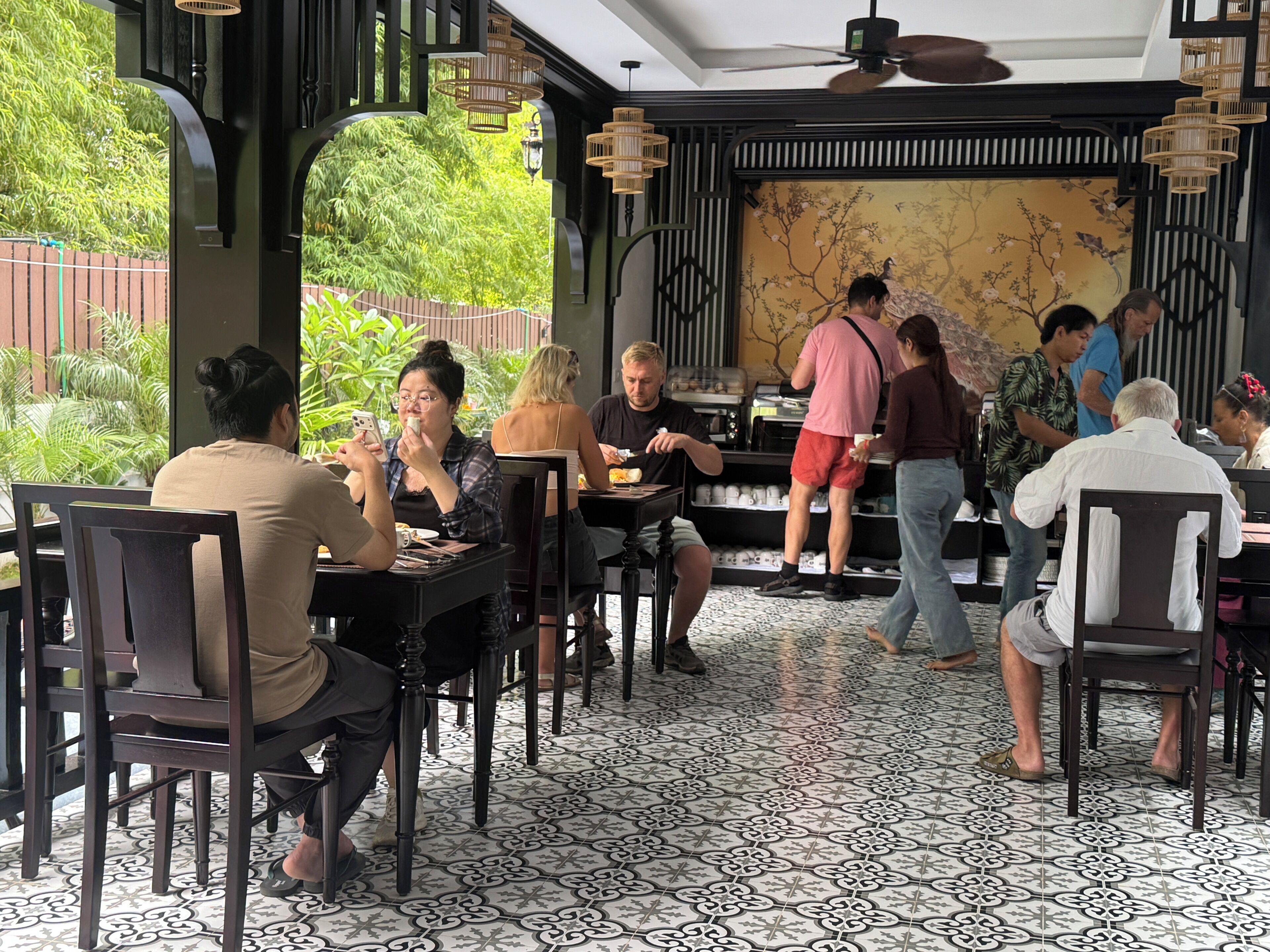 Un restaurante con mesas dentro, una barra de pedidos y vistas al exterior con vegetación.