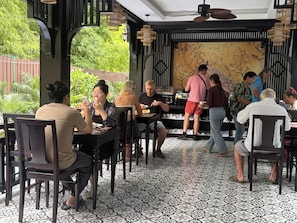 A restaurant with indoor seating, a counter for ordering, and a view of greenery outside. - Luang Prabang Indochine Heritage Hotel (Luang Prabang)