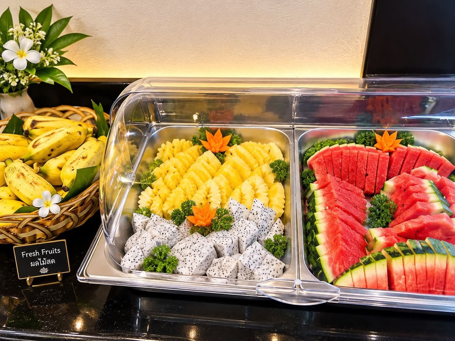 Un bufé con frutas frescas, incluyendo plátanos, piña, pitahaya y sandía.