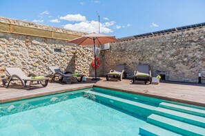 Ein Swimmingpool mit Liegestühlen und einem Rettungsring, umgeben von Steinmauern und einer Holzterrasse.