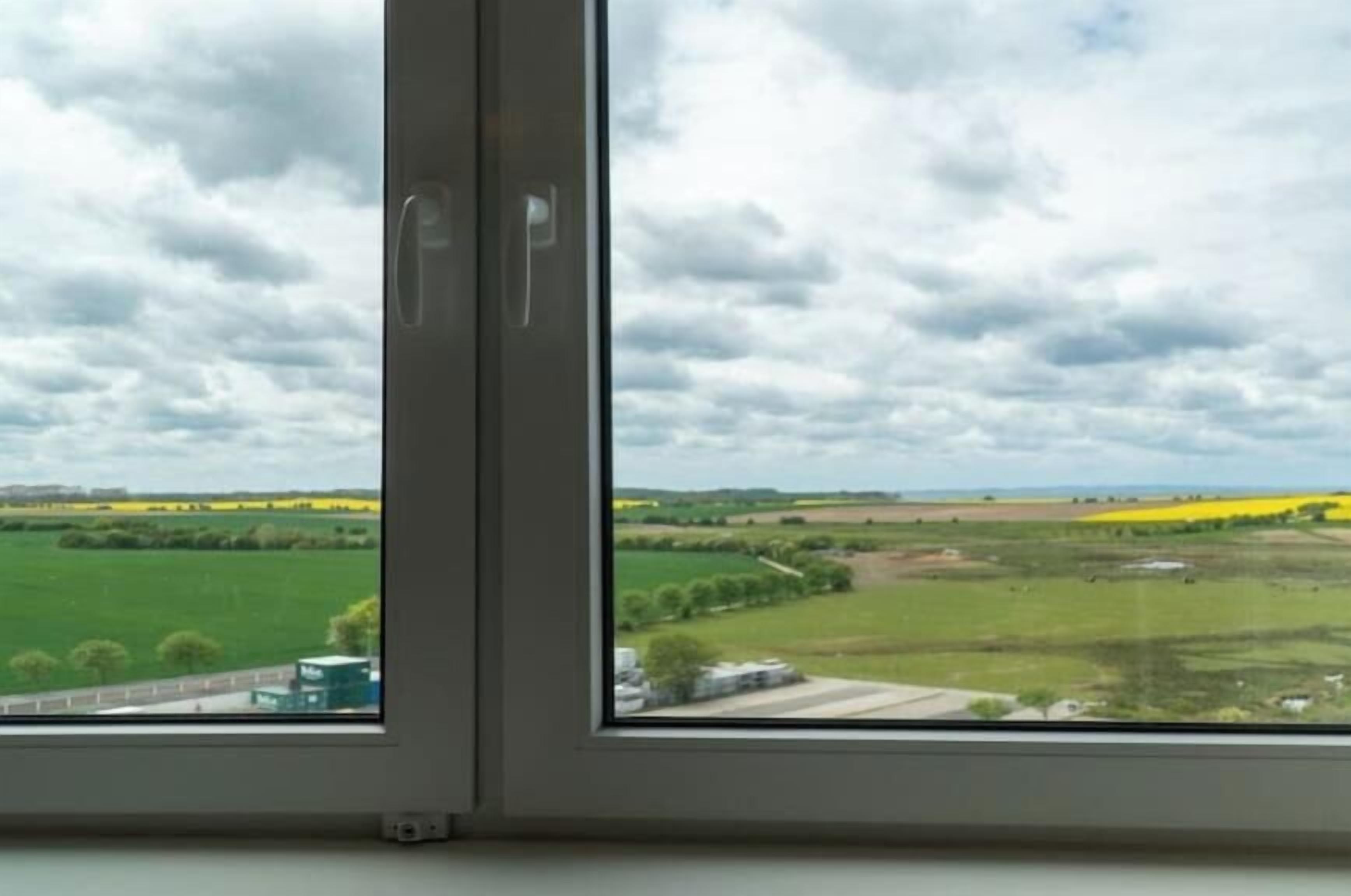 A window with a view of a rural landscape, including fields and a road.