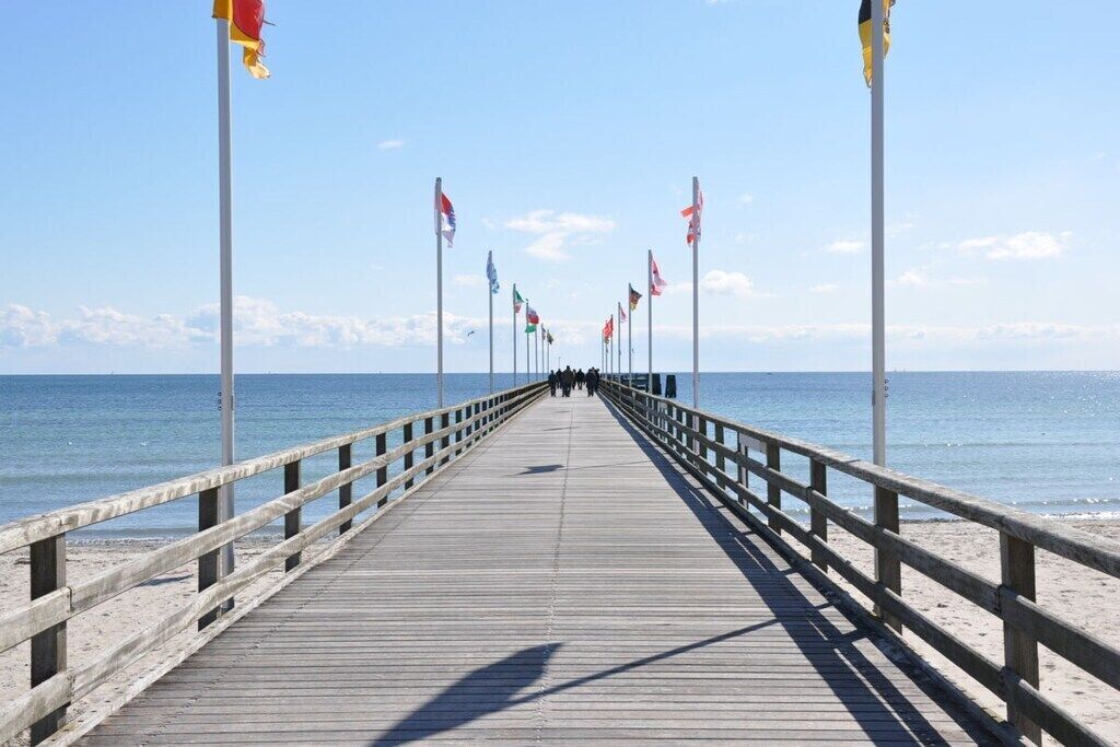 A wooden pier extending into the sea with multiple flags on poles.
