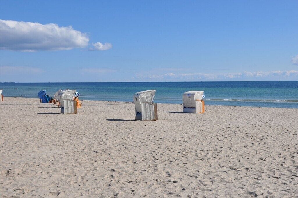 A beach with white beach chairs and a blue chair, a lifeguard stand, and the ocean in the background.