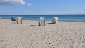 Une plage avec des chaises de plage blanches et une chaise bleue, un poste de surveillance pour les sauveteurs, et l’océan en arrière-plan.