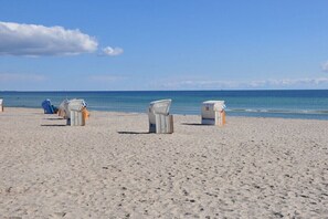 A beach with white beach chairs and a blue chair, a lifeguard stand, and the ocean in the background. - Holiday apartment with 2 bedrooms (Großenbrode)