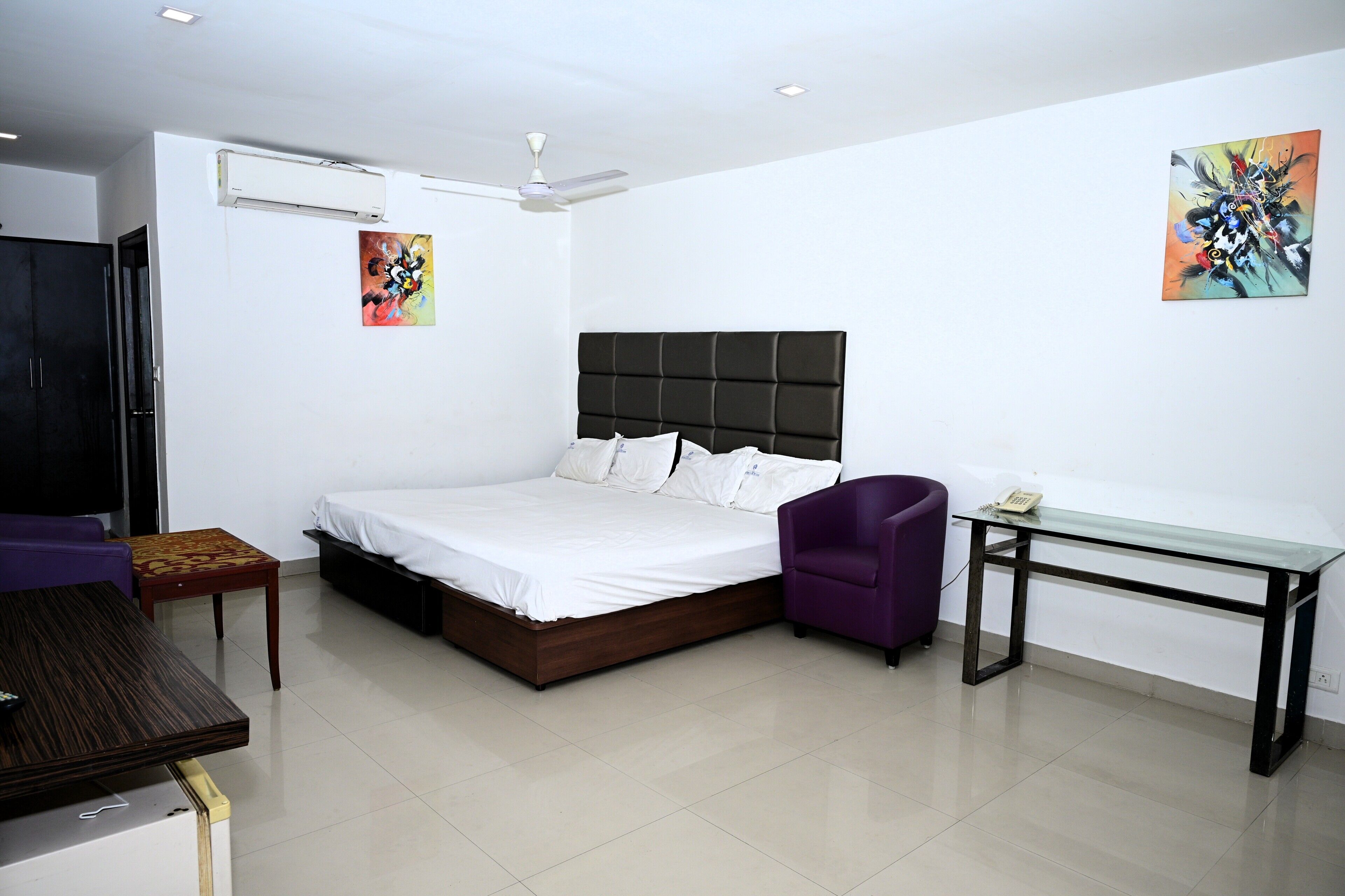 A hotel room with a bed, a desk, a chair, a wardrobe, and two paintings on the walls.