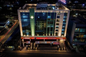 A modern building with a prominent glass facade, a vertical green accent, and multiple signage including 'ICICI Bank' and 'MURA GHAMBER'S'. - HOTEL SWAGATH INN (Vijayawada)