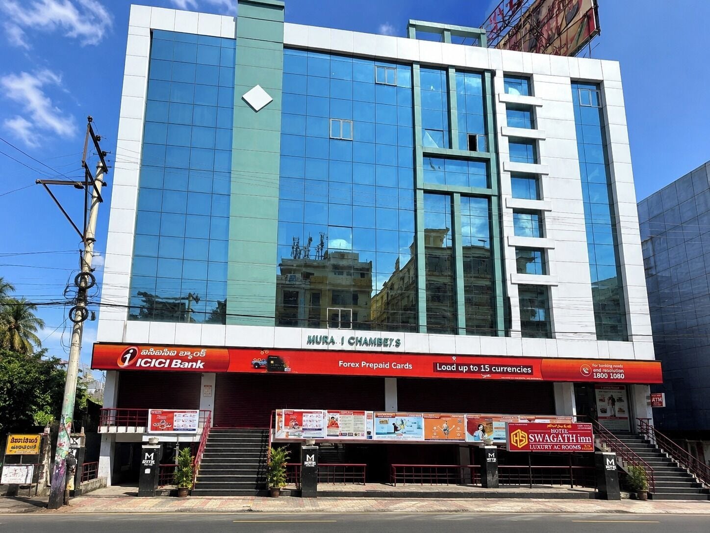 A modern building with a glass facade, a sign for ICICI Bank, and a SWAGATH hotel sign.