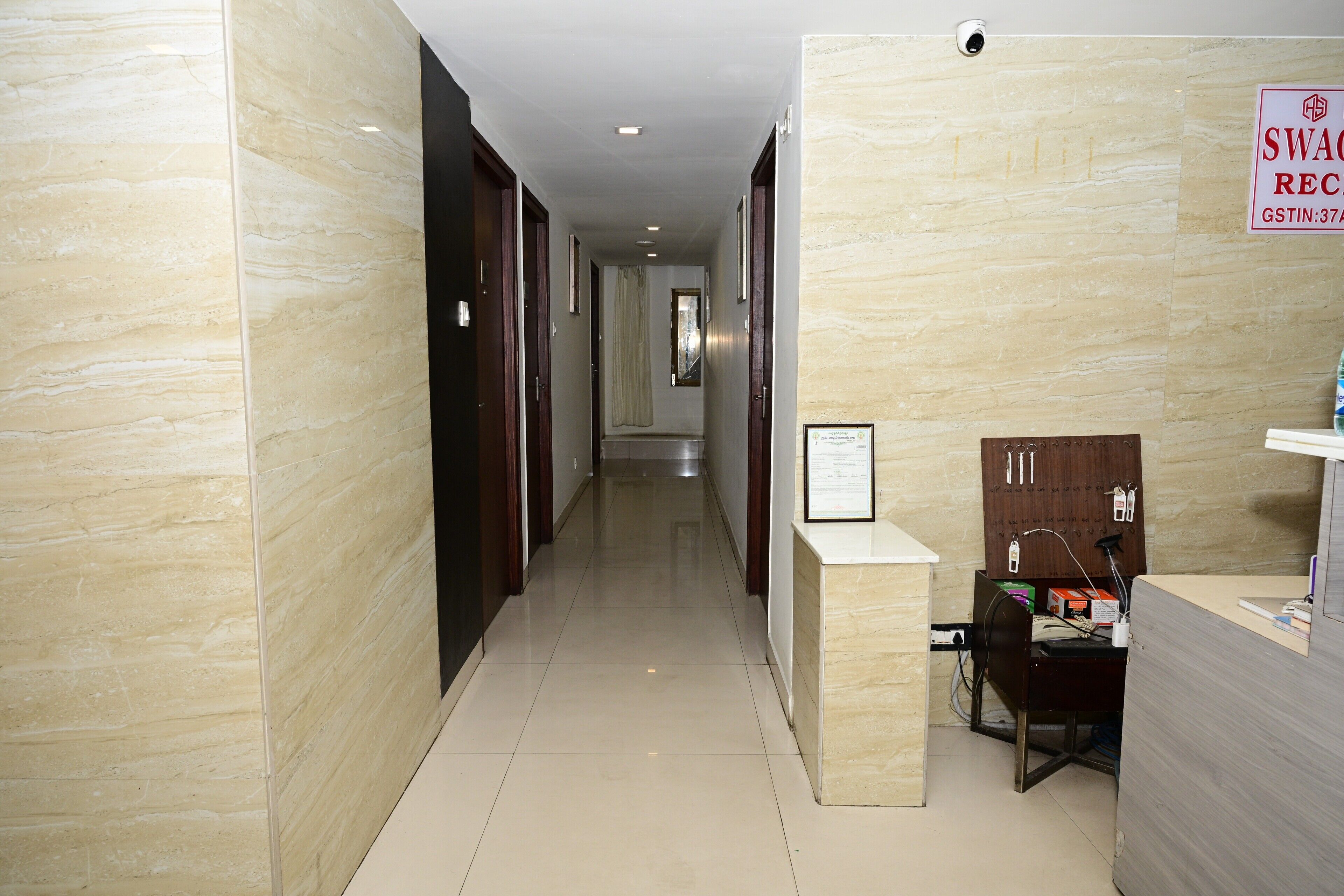 Zona de recepción de un hotel con un mostrador, una cámara de seguridad y un cartel con tarifas de habitaciones.