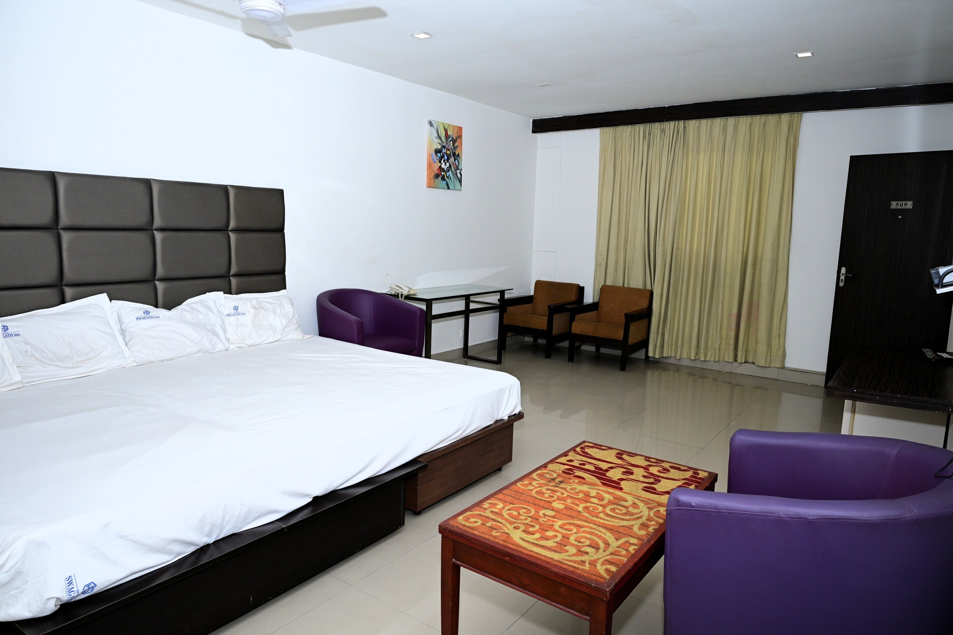 A hotel room with a bed, a desk, two chairs, a television, and a curtain.