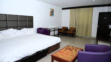 A hotel room with a bed, a desk, two chairs, a television, and a curtain.