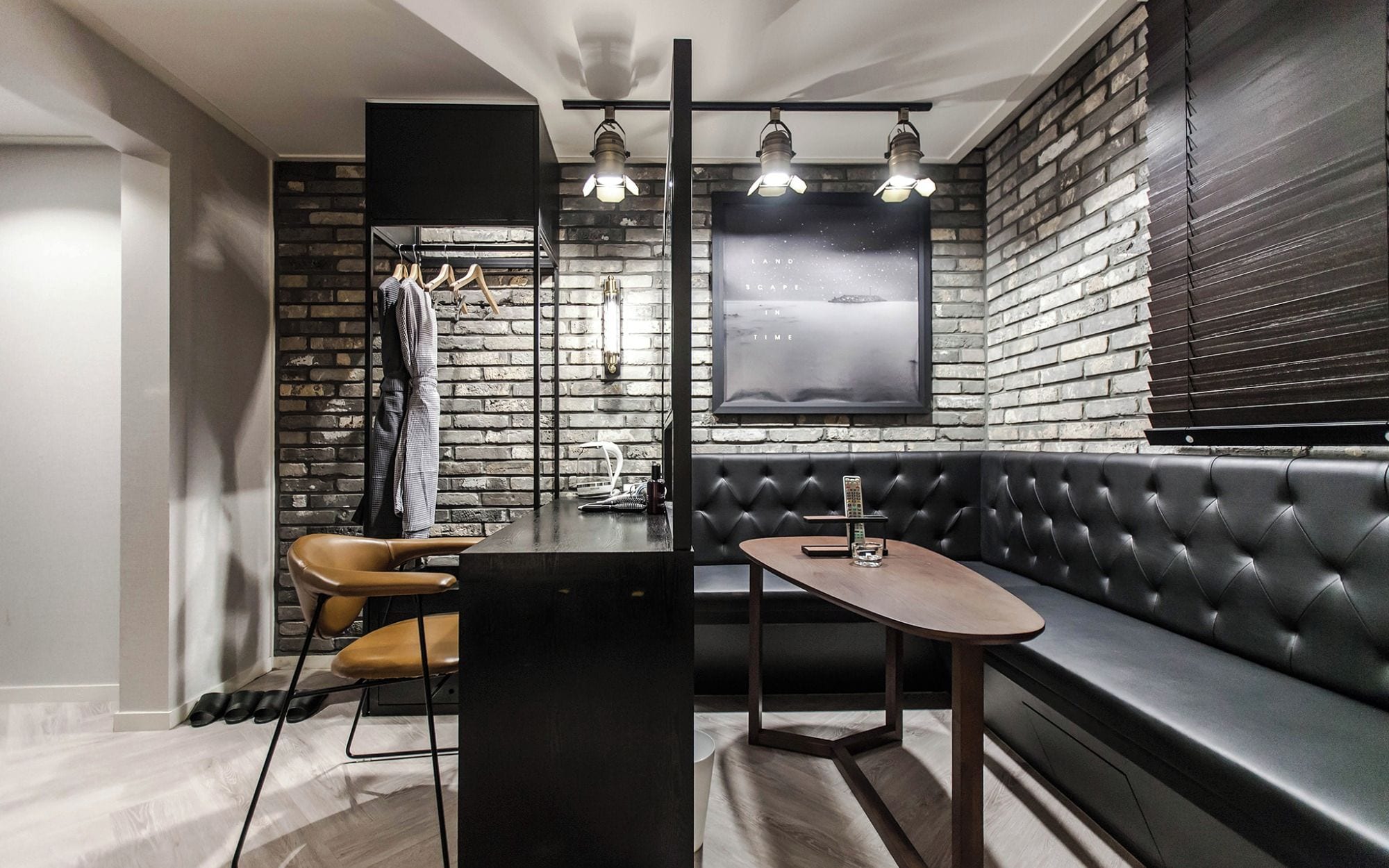 A modern interior with a black leather booth, a wooden table, and a brick wall.