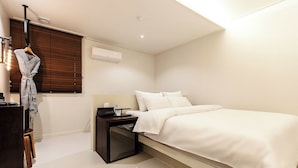 A hotel room with a bed, bedside table, and a hanging robe. - Hotel Yaja Daegu Seomun Market (Daegu)