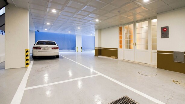 A parking garage with a white car parked in a lane, white walls, and a tiled ceiling.