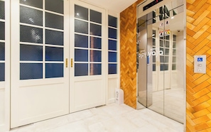 Entrada de un hotel con suelo de madera en dibujo de espiga, puertas dobles con paneles de vidrio y un letrero que indica un hotel.