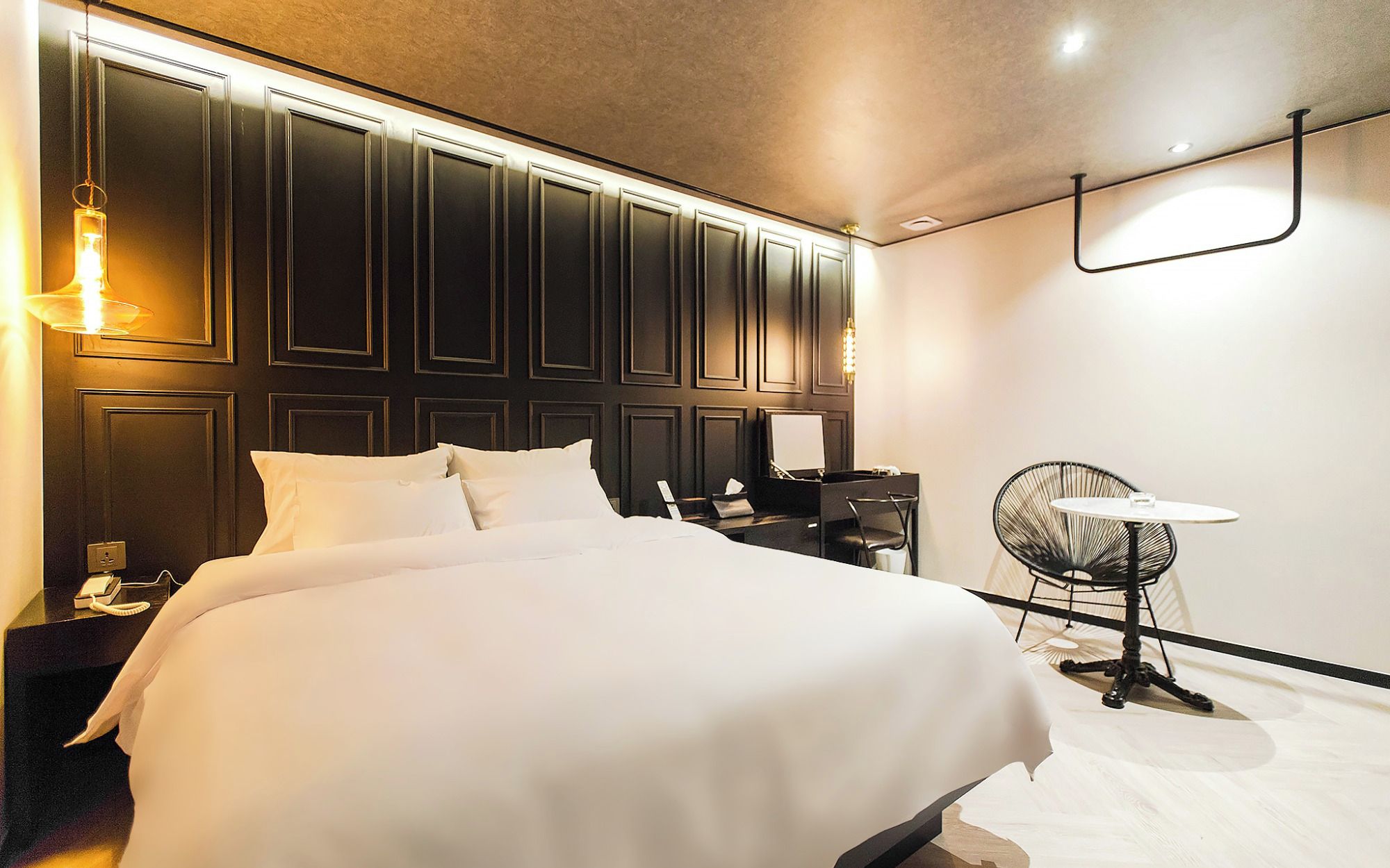 A hotel room with a large bed, a desk with a chair, a desk lamp, and a wall-mounted light fixture.