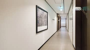 A hotel corridor with framed artwork on the walls, a sign indicating guest rooms, and a door labeled '80S'.