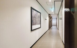 Hotelgang med indrammede kunstværker på væggene, et skilt der viser hen til gæsteværelser og en dør med teksten '80S'.
