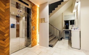 Un vestíbulo de hotel con una escalera, una recepción e indicaciones hacia habitaciones de huéspedes y un estacionamiento.