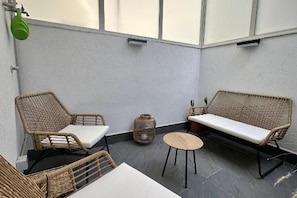 Ein Balkon mit Korbmöbeln, darunter zwei Stühle, ein Sofa, ein kleiner runder Tisch und ein Korbkorb.
