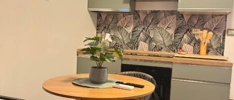 Una cocina compacta con una mesa redonda, una planta en maceta y un lavavajillas empotrado.