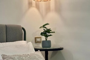 Ein Zimmer mit einem Bett, einem Nachttisch mit Pflanze und einer Wandleuchte.