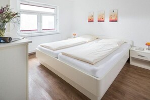 Ein sauberes, modernes Schlafzimmer mit Doppelbett, Nachttischen, einem kleinen Schreibtisch und einem Fenster mit Jalousien.