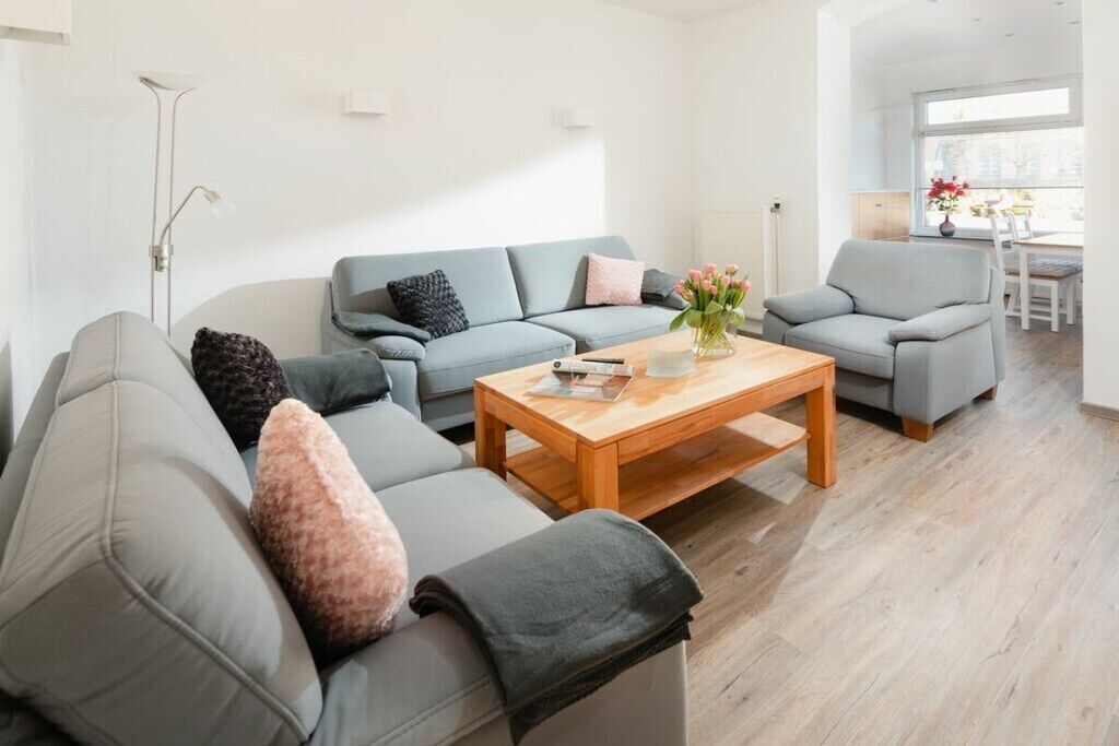 Ein modernes Wohnzimmer mit einem grauen Sofagarnitur, einem Holztisch und einer Vase mit Blumen.