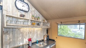 A compact kitchen with a wooden wall, a clock, shelves with decorative items, a sink, and a window with a view. - Luxury Waterfront Safari Lodge (Almere)