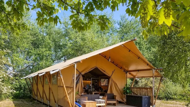 A tented accommodation with a deck, seating area, and a small table. - Luxury Waterfront Safari Lodge (Almere)