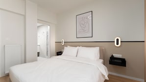 A modern hotel room with a large bed, a nightstand, a wall-mounted light, and a framed abstract art piece. - Luxury 4Bedrooms Stay in North Athens (Agia Paraskevi)