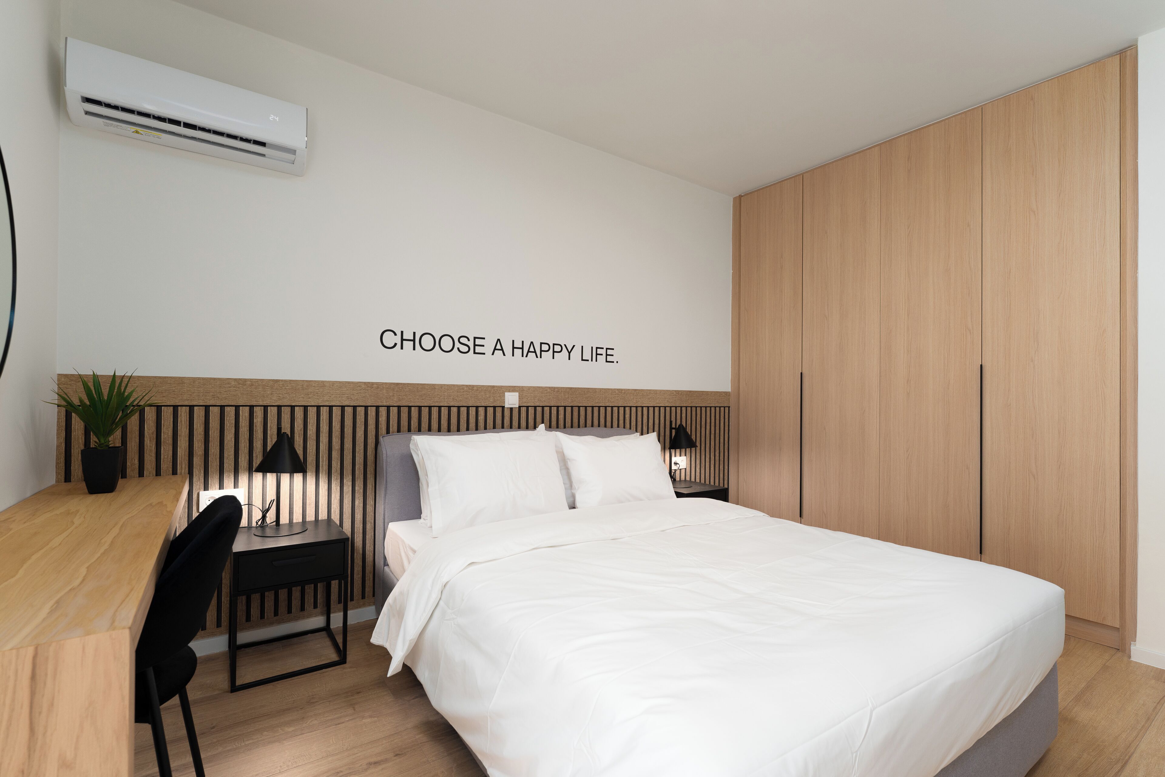 A modern bedroom with a bed, bedside tables, a desk, and a potted plant.