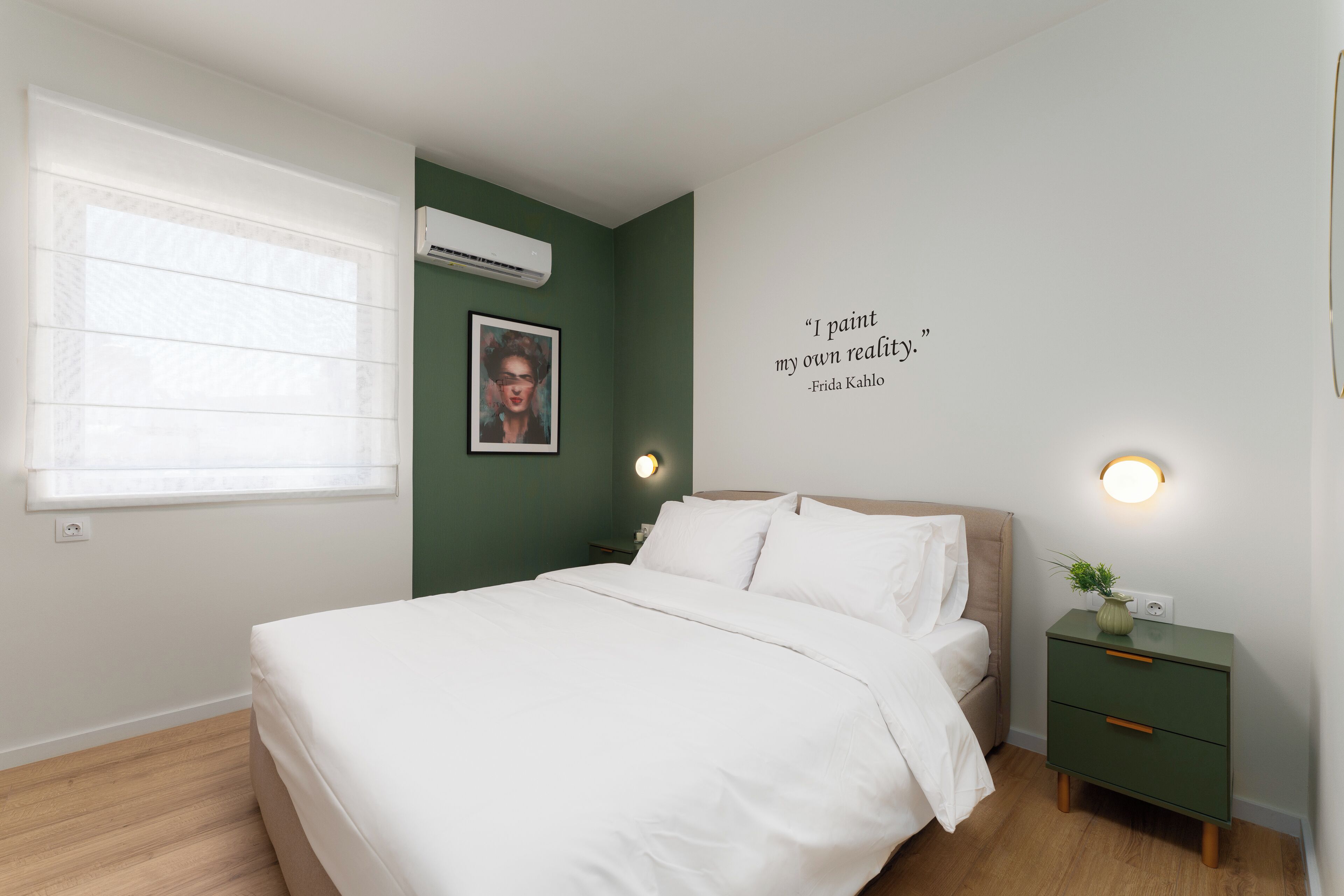 Ein Schlafzimmer mit Bett, Nachttisch, Wandklimaanlage, gerahmtem Bild und einem motivierenden Zitat.