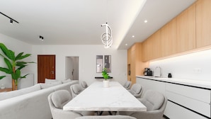 A modern kitchen with white cabinets, a marble countertop, and a dining area with a white table and grey chairs. - Luxury 4Bedrooms Stay in North Athens (Agia Paraskevi)