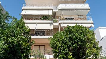 Un immeuble résidentiel à plusieurs étages, doté de balcons, avec un ciel dégagé et entouré de verdure.