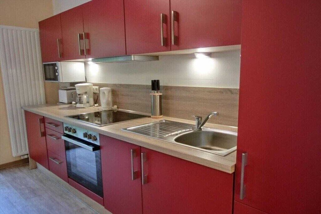 A kitchen with red cabinets, stainless steel appliances, and a double sink.