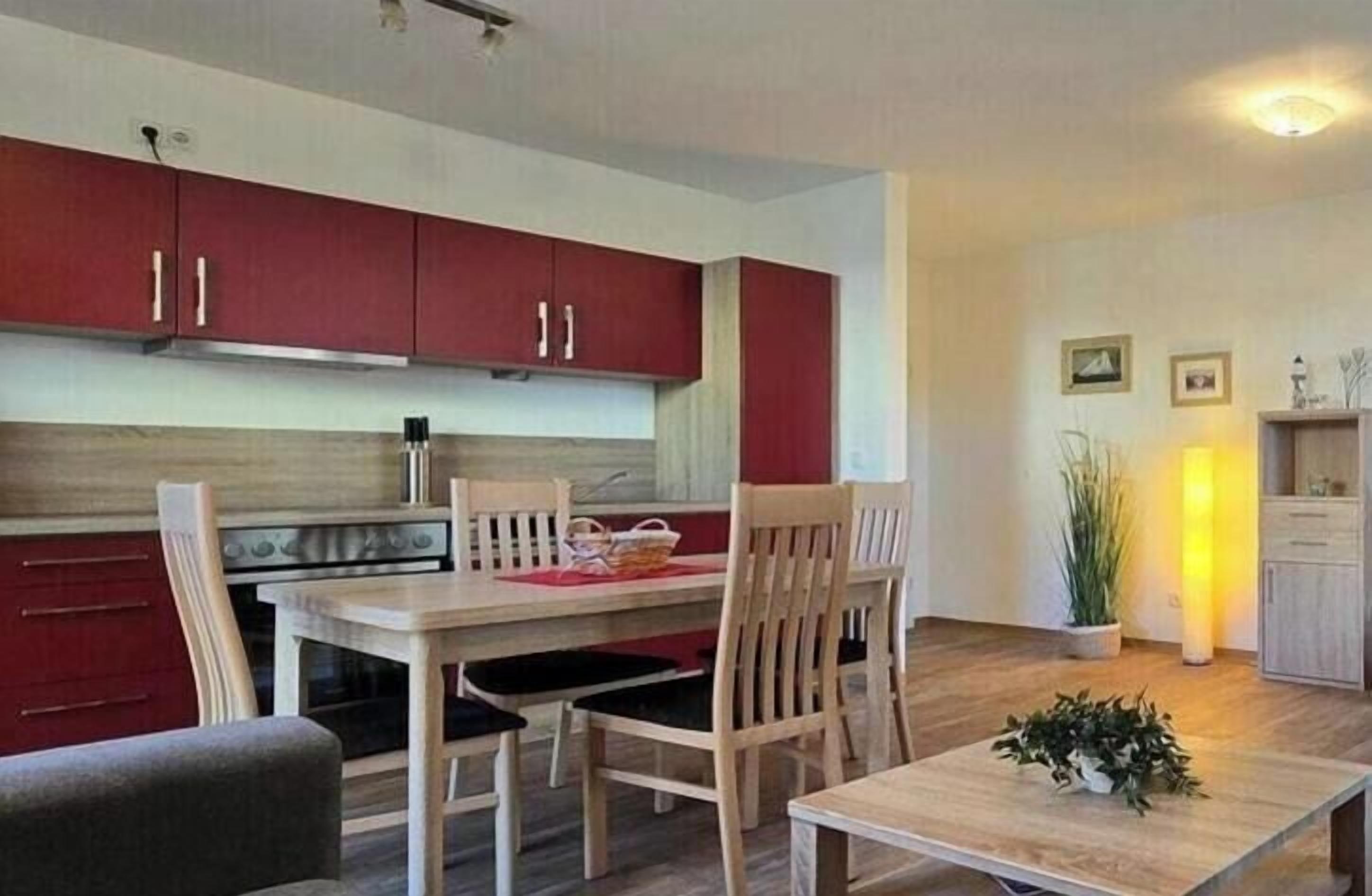 Una cocina moderna con armarios rojos, una mesa de comedor con sillas y un pequeño rincón comedor con una planta.
