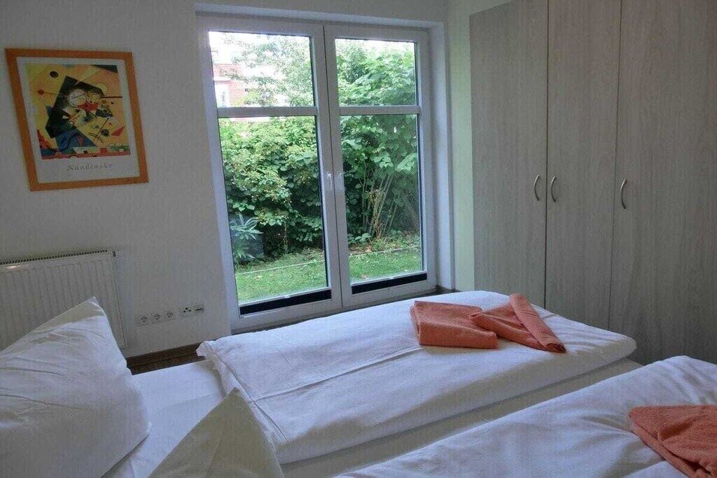 A bedroom with two beds, a window with a view of greenery, and a wardrobe.