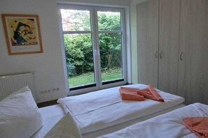 A bedroom with two beds, a window with a view of greenery, and a wardrobe. - Holiday apartment L39 (Graal-Müritz)