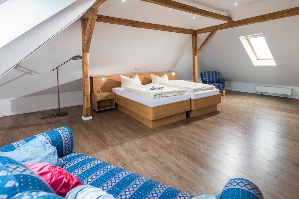 Une chambre avec un plafond en pente, des poutres en bois, un lit avec des oreillers, une chaise et une lampe sur pied.