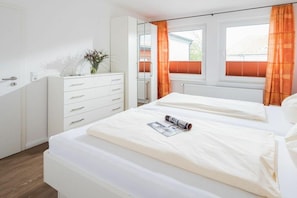 Ein Schlafzimmer mit zwei Betten, einem Schminktisch, einem Spiegel und einem Fenster mit Vorhängen.