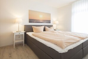 Een slaapkamer met een bed, twee nachtkastjes, een lade en een schilderij aan de muur.
