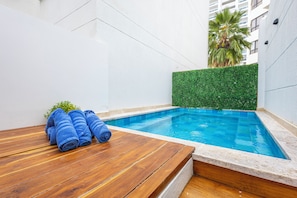 Ein kleiner Pool mit einer Holzterrasse und einer Hecke.