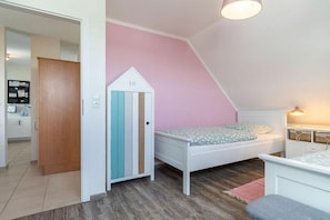 Ein Schlafzimmer mit schrägem Dach, einem Bett mit gemustertem Matratze, einer kleinen weißen Kommode und einer Tür mit Streifenmuster.