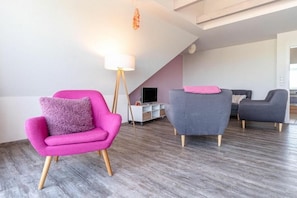 Ein modernes Wohnzimmer mit einem rosa Sessel, einem grauen Sessel und einem grauen Sofa.