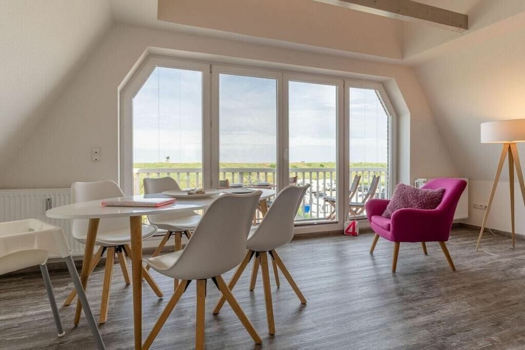 Un coin repas avec une table et des chaises, une vue dégagée grâce à de grandes fenêtres et une chaise rouge.