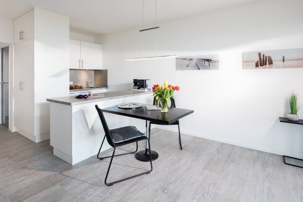Eine moderne Küche mit weißen Schränken, einem Esstisch mit Blumenvase und Bildern an der Wand.