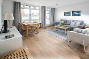 Ein modernes Wohnzimmer mit Essbereich, einer Couch, einem Couchtisch und einem Fernseher auf einem Schrank.